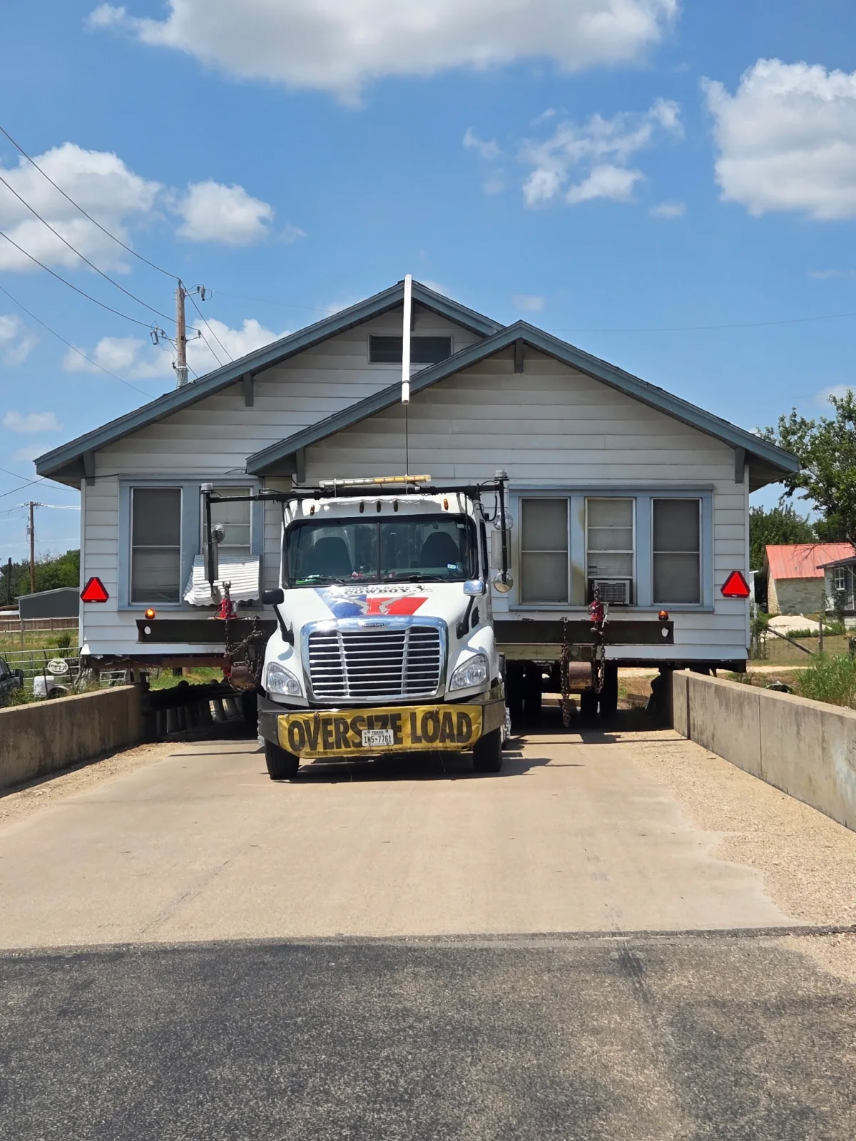 Cowboy House Movers guiding a house across a narrow bridge